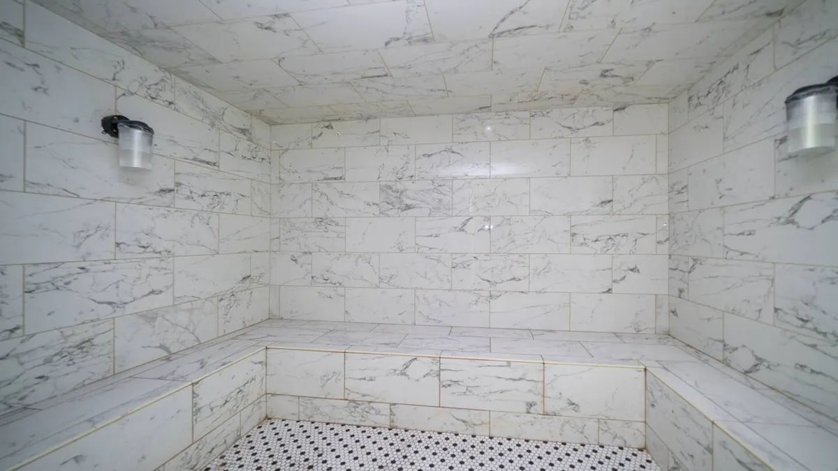 This image highlights a sophisticated steam room with marble walls, a textured floor, and soft ambient lighting. The luxurious setting is designed for relaxation and rejuvenation after a long day.