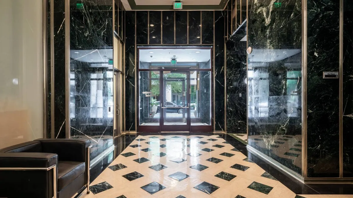 A sophisticated lobby interior featuring a black leather chair, diamond-patterned floor, and glass entrance doors. The space is designed for both waiting and conducting business, with a modern and inviting atmosphere that hints at the property's professional environment.