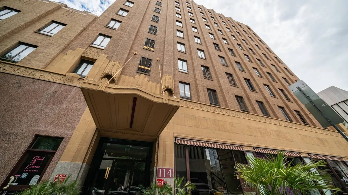 This is an exterior shot showing the building’s architectural details, featuring an entrance awning and large windows that offer a glimpse into the urban lifestyle. The image captures the building within its city context, inviting exploration of the nearby vibrant downtown area.