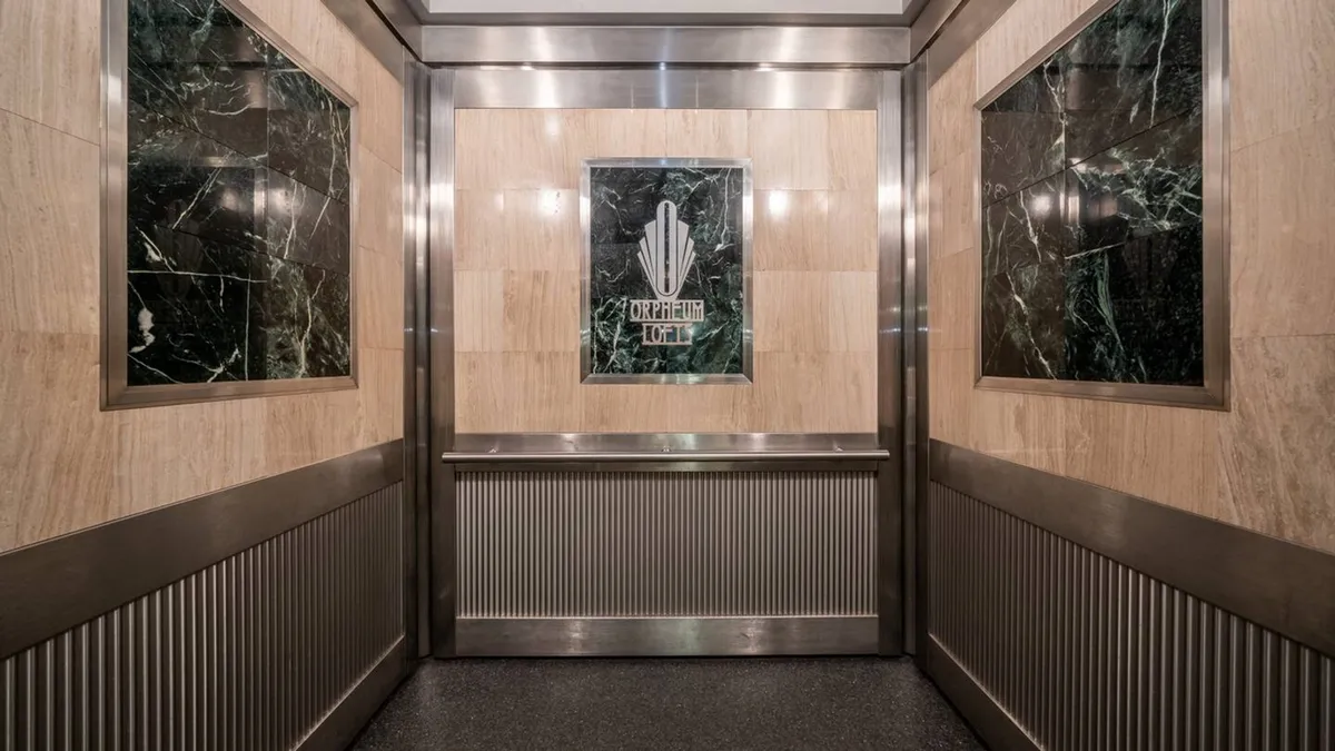 This image features a sophisticated building lobby with marble walls, metal accents, and an elevator sign. The setting provides a sense of both arrival and anticipation, capturing the transition from home to adventure and back again.