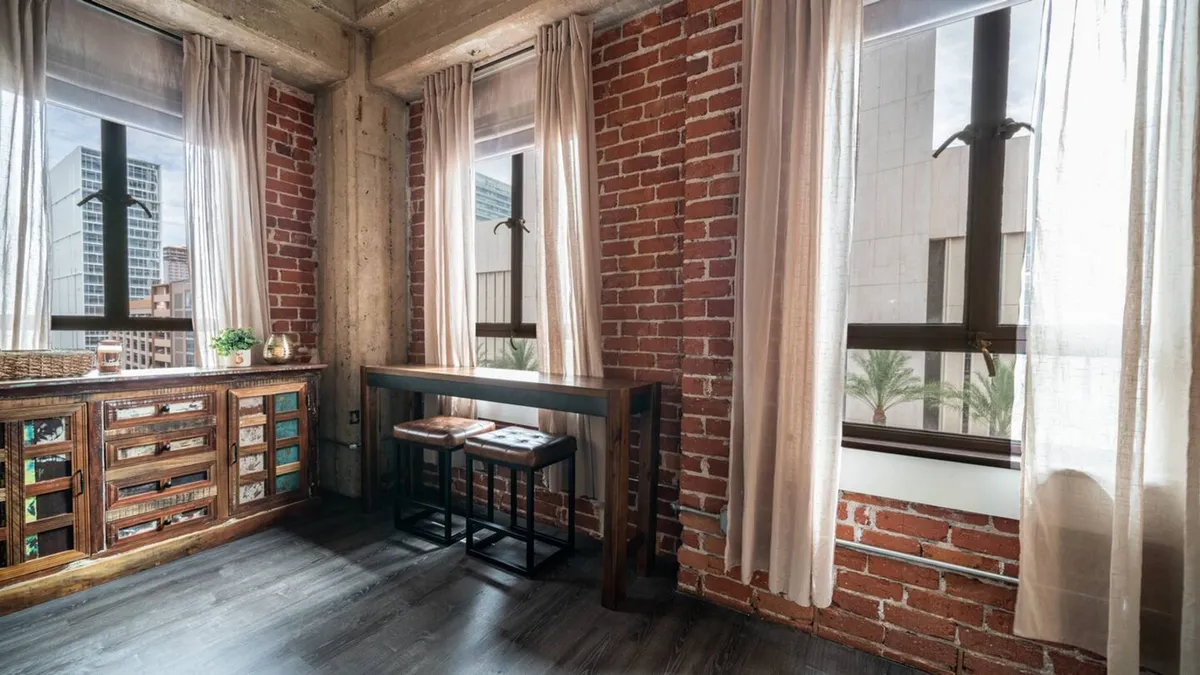 A calm workspace with a wooden cabinet, desk, and large windows overlooking the city. The space offers natural light and a view, ideal for working, reading, or relaxing breaks.