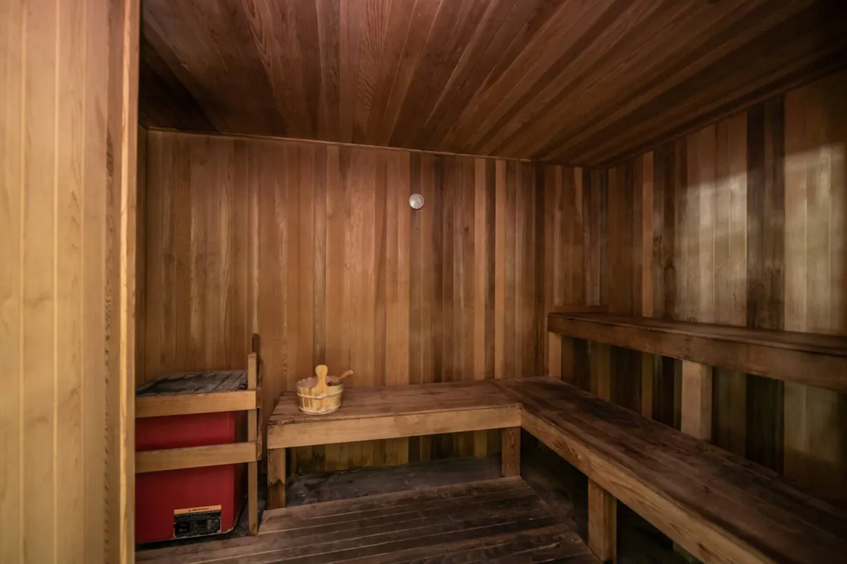 A tranquil sauna interior is presented, with wooden benches, a classic sauna bucket and ladle, and a visible temperature gauge. The space exudes warmth and invites moments of solitude or social connection.