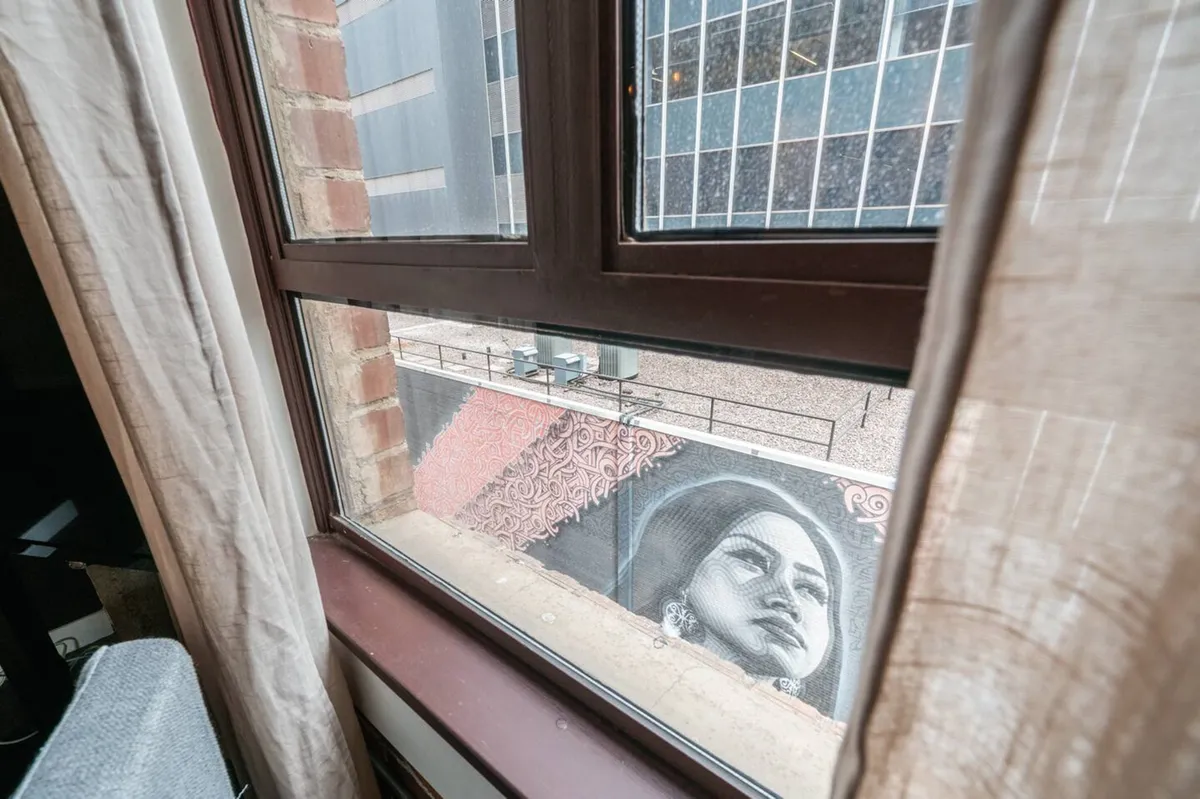 The image features a large, colorful mural inside, with a window framing an urban landscape outside. The scene blends artistic inspiration with views of the dynamic neighborhood, suggesting access to local creativity just steps away from the residence.