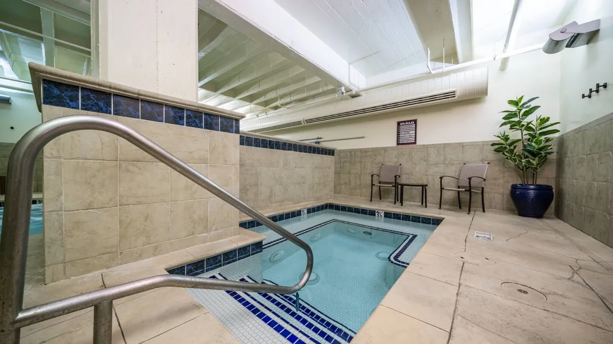 A cozy jacuzzi area is shown here, with a bubbling hot tub, inviting chairs, a safety railing, and a leafy plant adding a touch of nature. The ambiance is calm and perfect for unwinding.