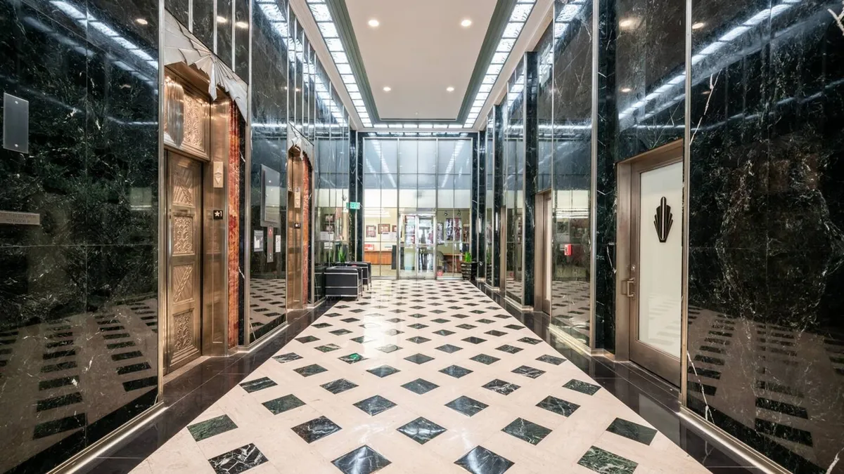 The image showcases a luxurious, modern lobby with polished marble floors, elegant elevators, floor-to-ceiling glass entrance, and intricate wall designs, creating a sophisticated first impression for guests as they enter the downtown Phoenix loft building.